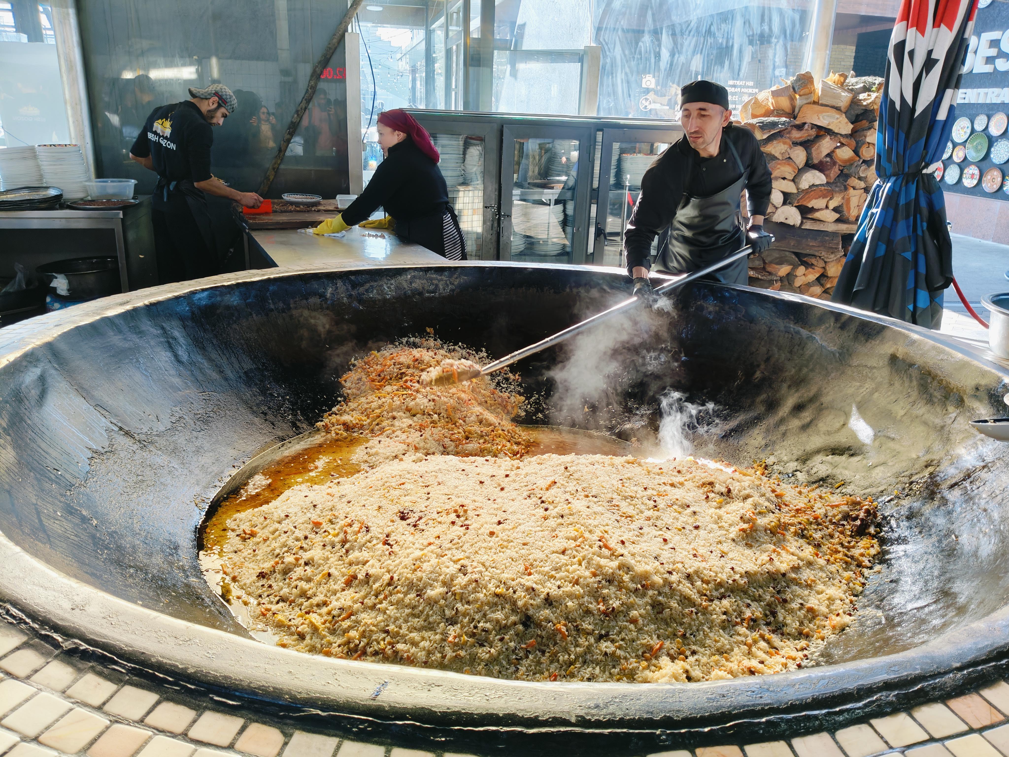 Traditional plov preparation in massive kazan at Besh Quzon in Tashkent - authentic Uzbek national rice dish being cooked in huge cauldrons for communal dining experience